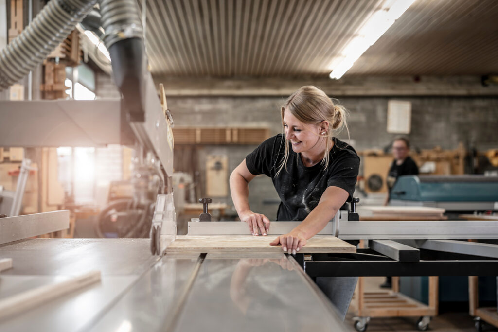 junge Frau als Schreiner sägt an der Kreissäge eine Holzplatte