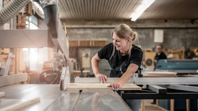 junge Frau als Schreiner sägt an der Kreissäge eine Holzplatte